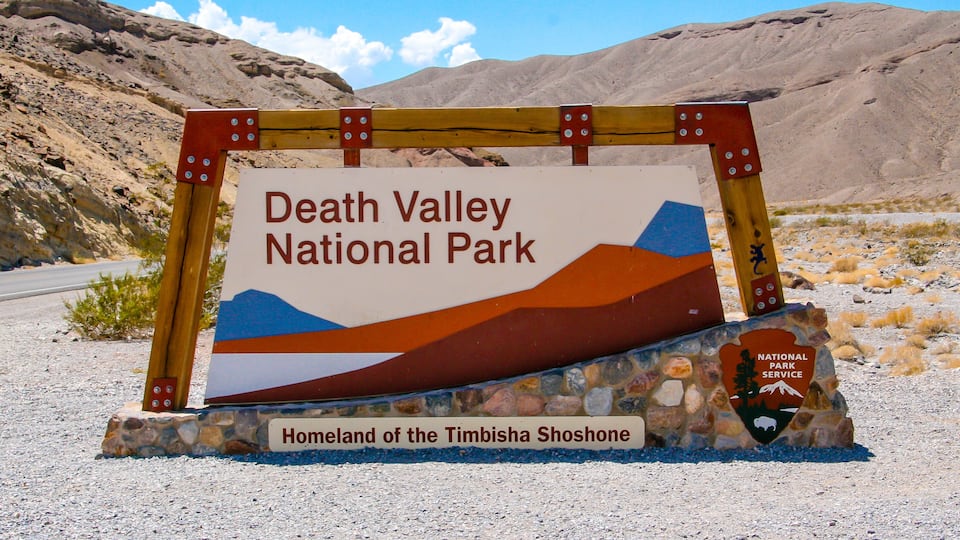 A sign for Death Valley National Park with a mountainous landscape in the background.