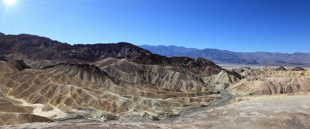 A desert landscape with rugged, eroded hills and distant mountains under a clear blue sky.