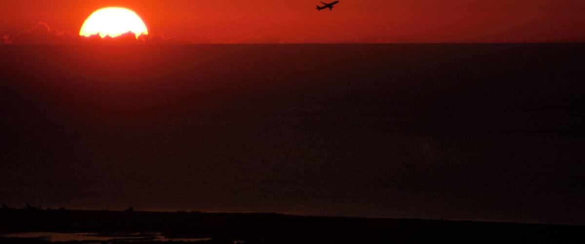A sunset over a body of water with an airplane flying in the distance.