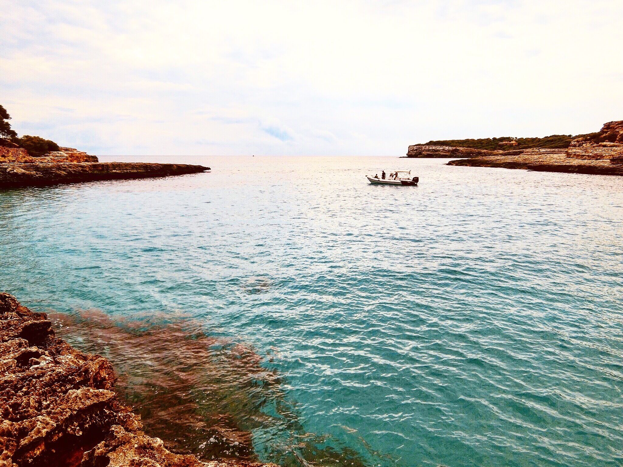 A calm sea with rocky shores and a small boat in the distance.