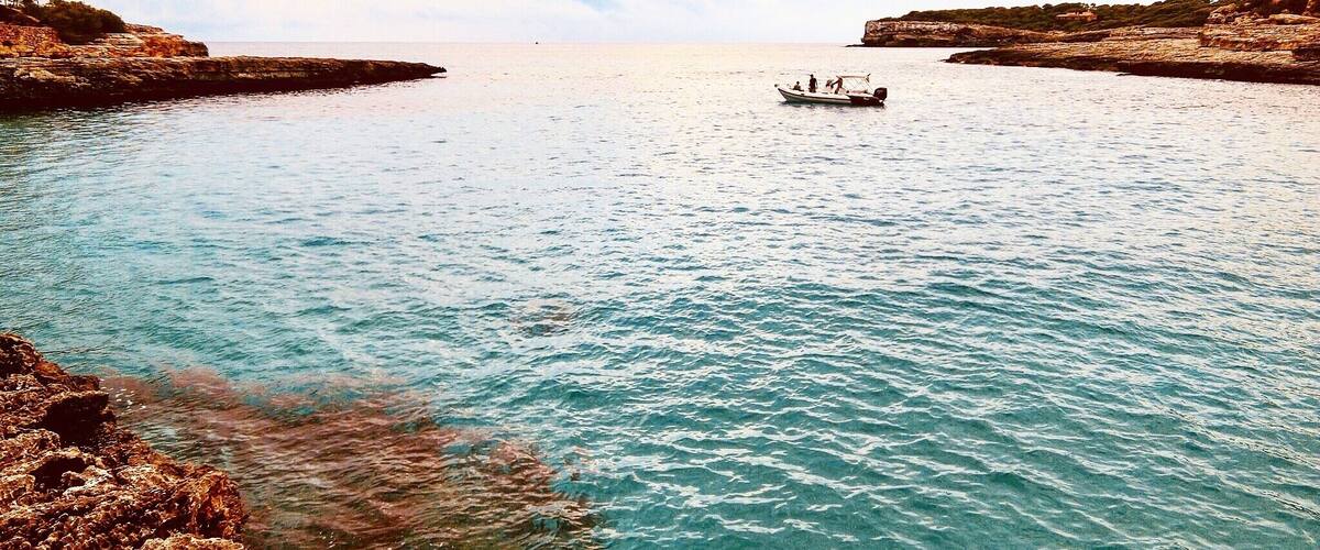A calm sea with rocky shores and a small boat in the distance.