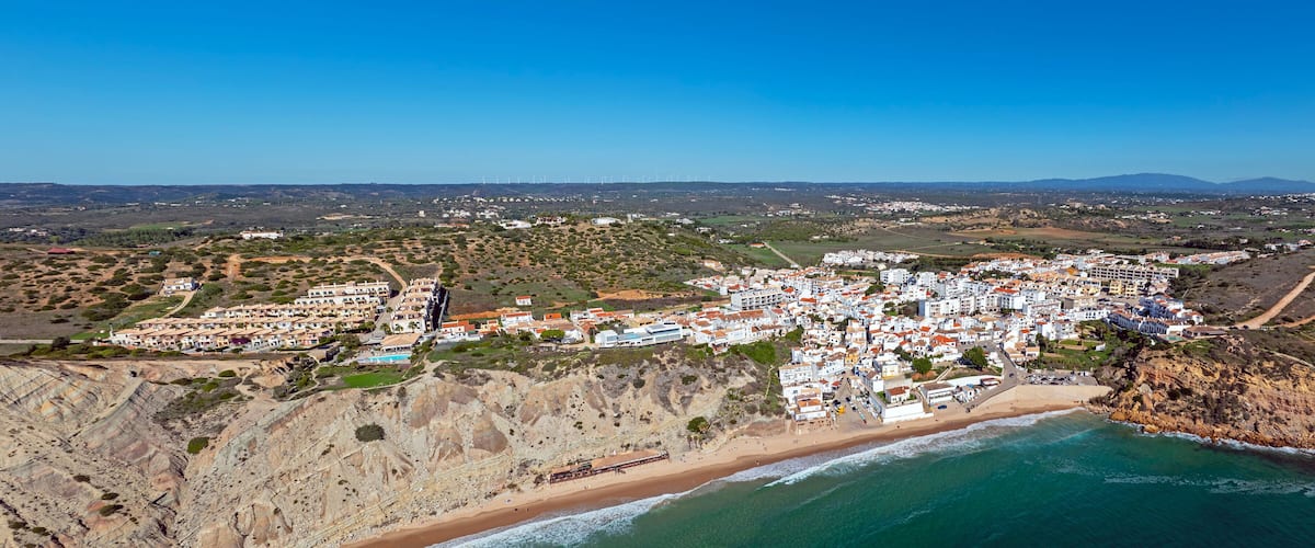 A coastal town with a beach, buildings, and wind turbines in the background.