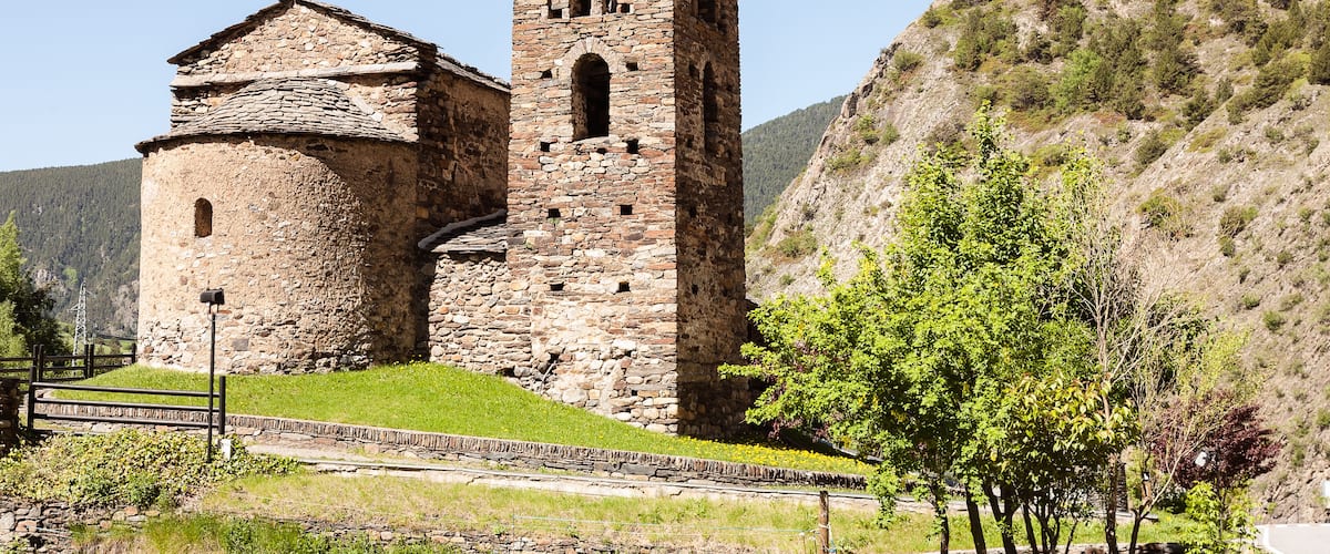 A stone church with a bell tower and a small dome, surrounded by a hilly landscape with sparse vegetation.