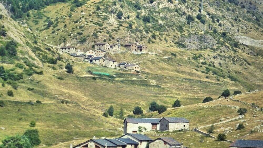 Un village rural niché dans une vallée, avec une colline imposante en arrière-plan.