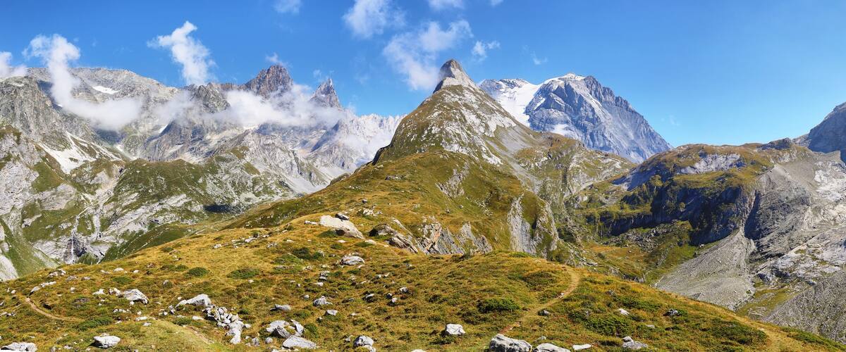 A mountain peak with a distinct conical shape, surrounded by rugged, snow-capped mountains and a clear blue sky.