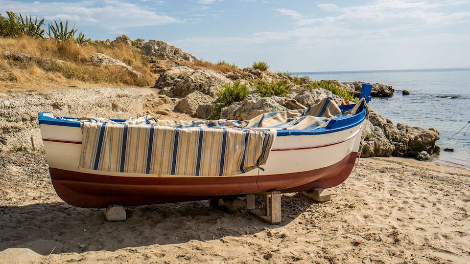 A small boat on a sandy beach with rocky terrain and a clear sky.