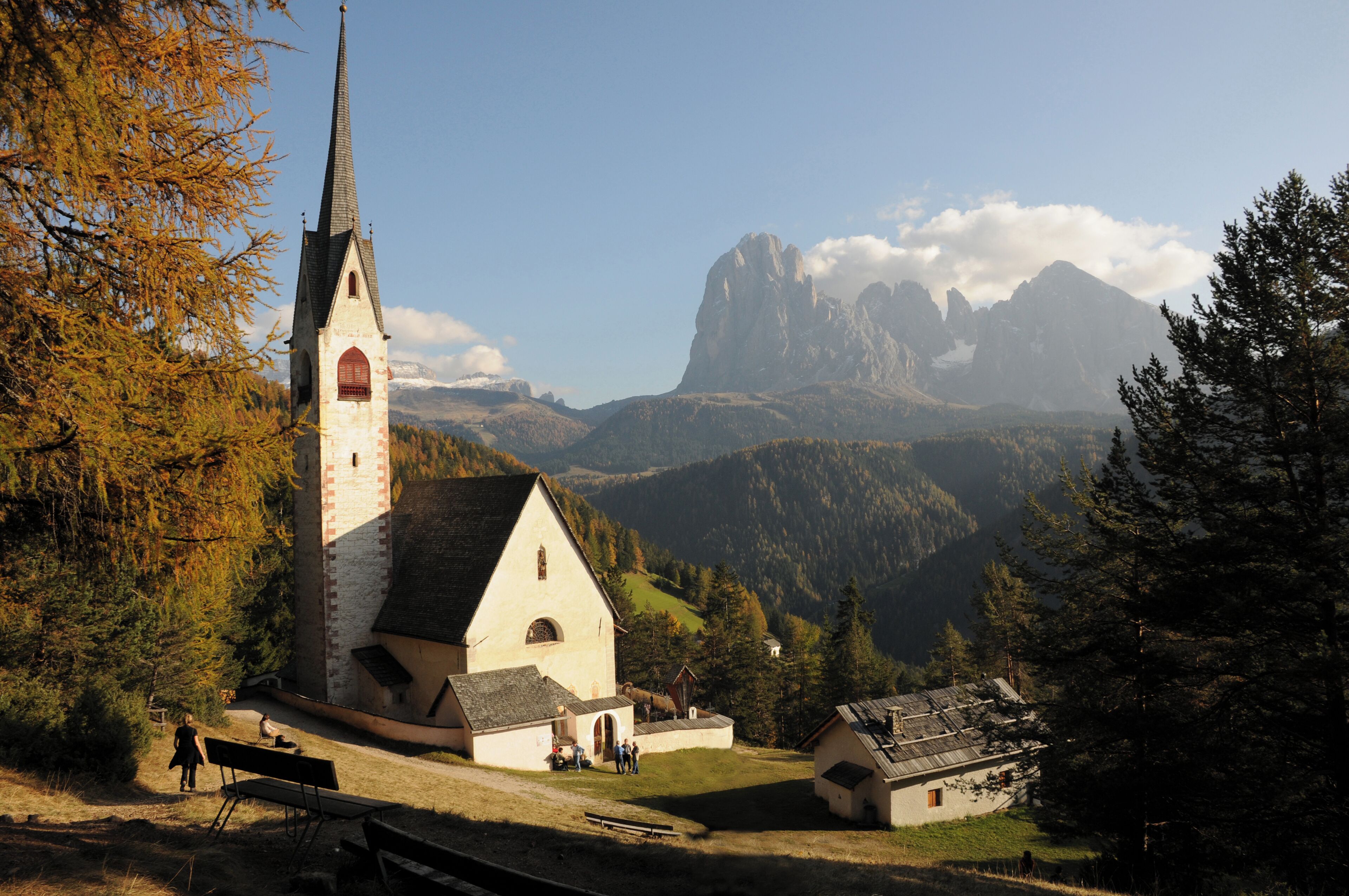 A church with a tall steeple, surrounded by autumn trees and mountains in the background.