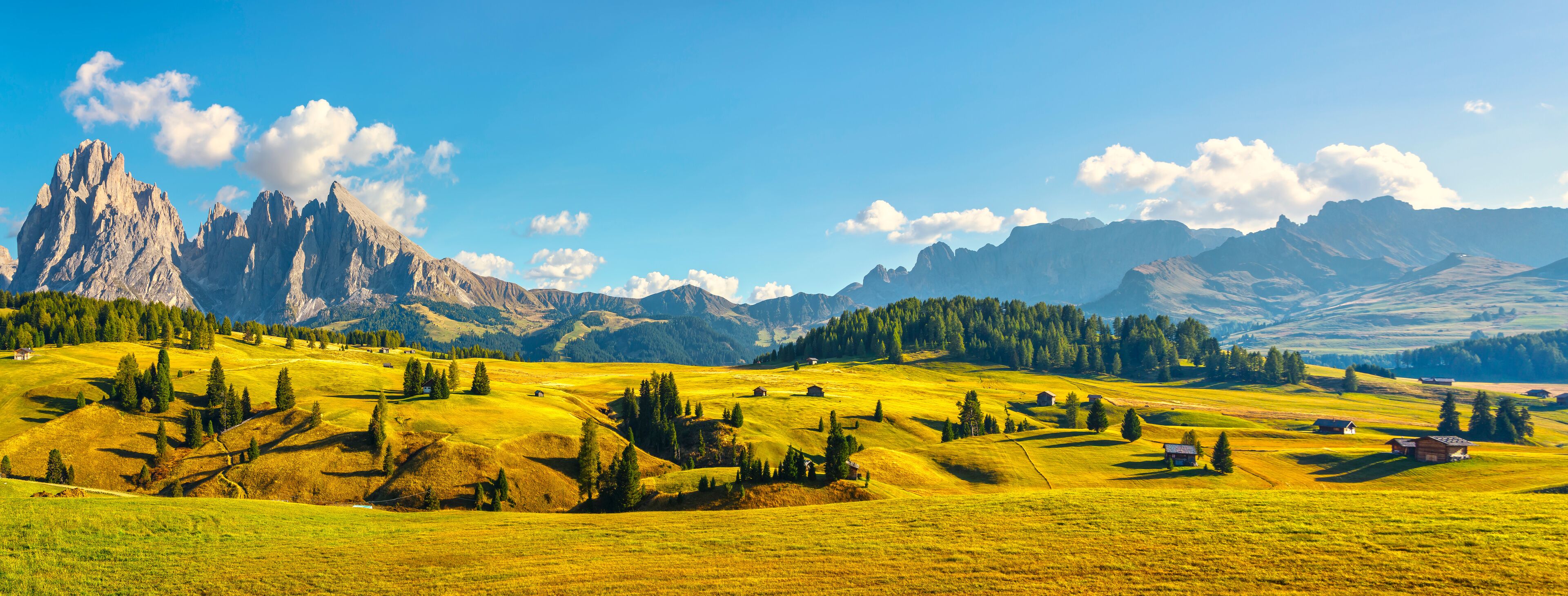 A mountainous landscape with green fields, scattered trees, and a prominent rocky peak.