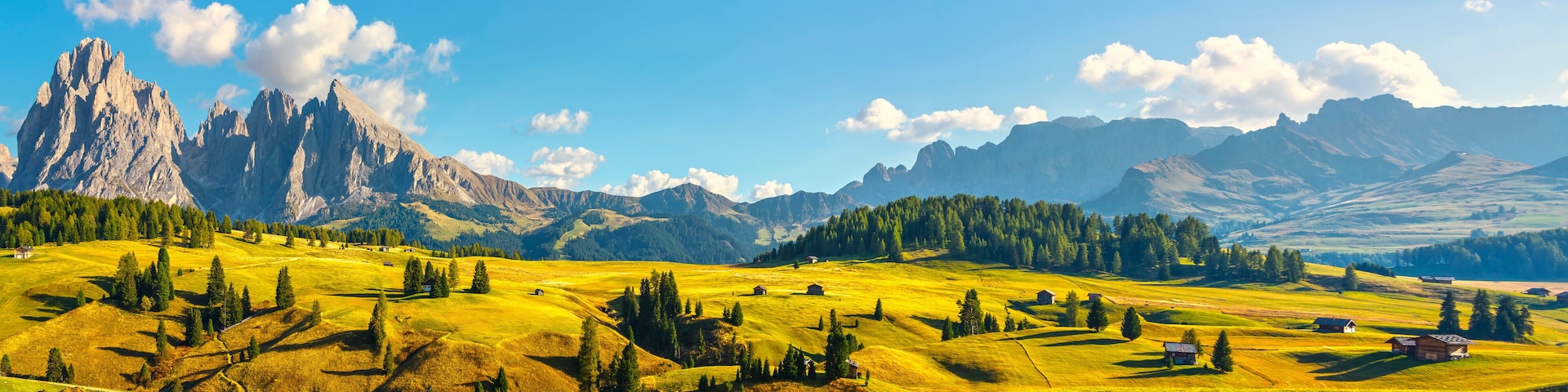 A mountainous landscape with green fields, scattered trees, and a prominent rocky peak.