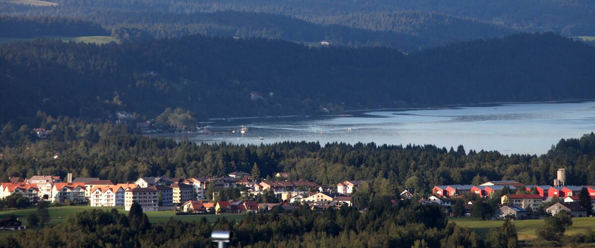 A lakeside town with red-roofed buildings, surrounded by dense forests and rolling hills.