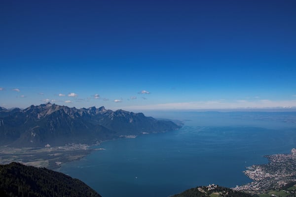 Eine gebirgige Landschaft mit einem großen Gewässer im Vordergrund und einer Stadt auf der rechten Seite.