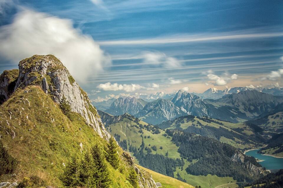 A mountain landscape with a prominent rocky peak, lush green valleys, and a distant lake.