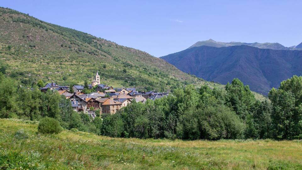 A village nestled in a valley with mountains in the background.