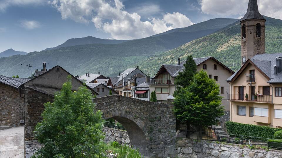 A stone bridge, houses, and a church tower in a mountainous village.