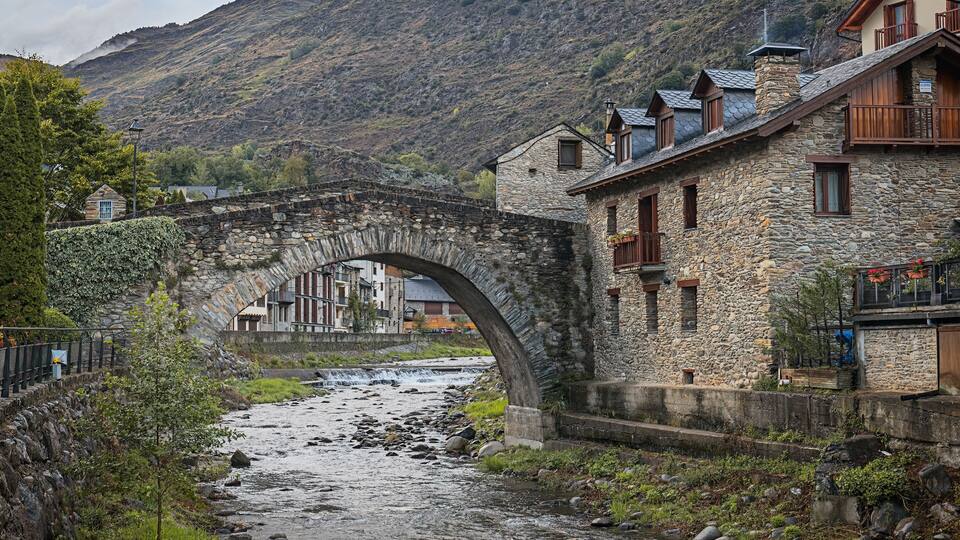 A stone bridge over a river, surrounded by stone buildings and a mountainous landscape.