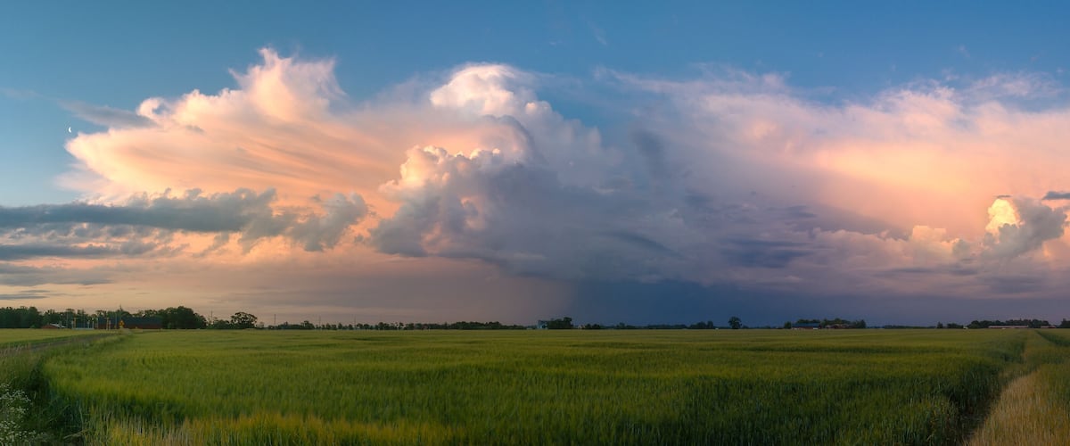 A vast green field with a dramatic sky filled with clouds.