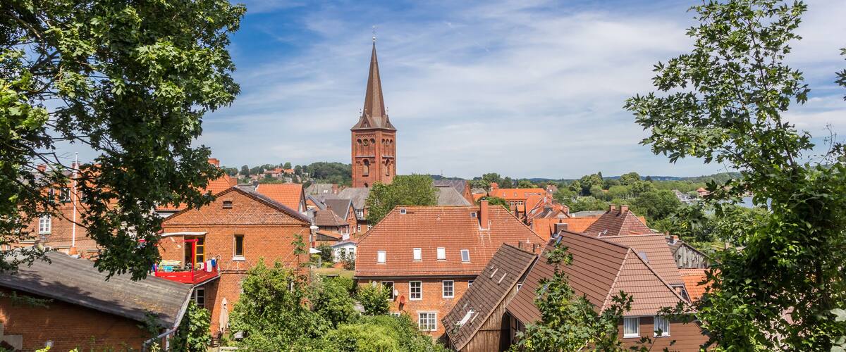 A town with red-roofed houses, a prominent church tower, and lush green trees.