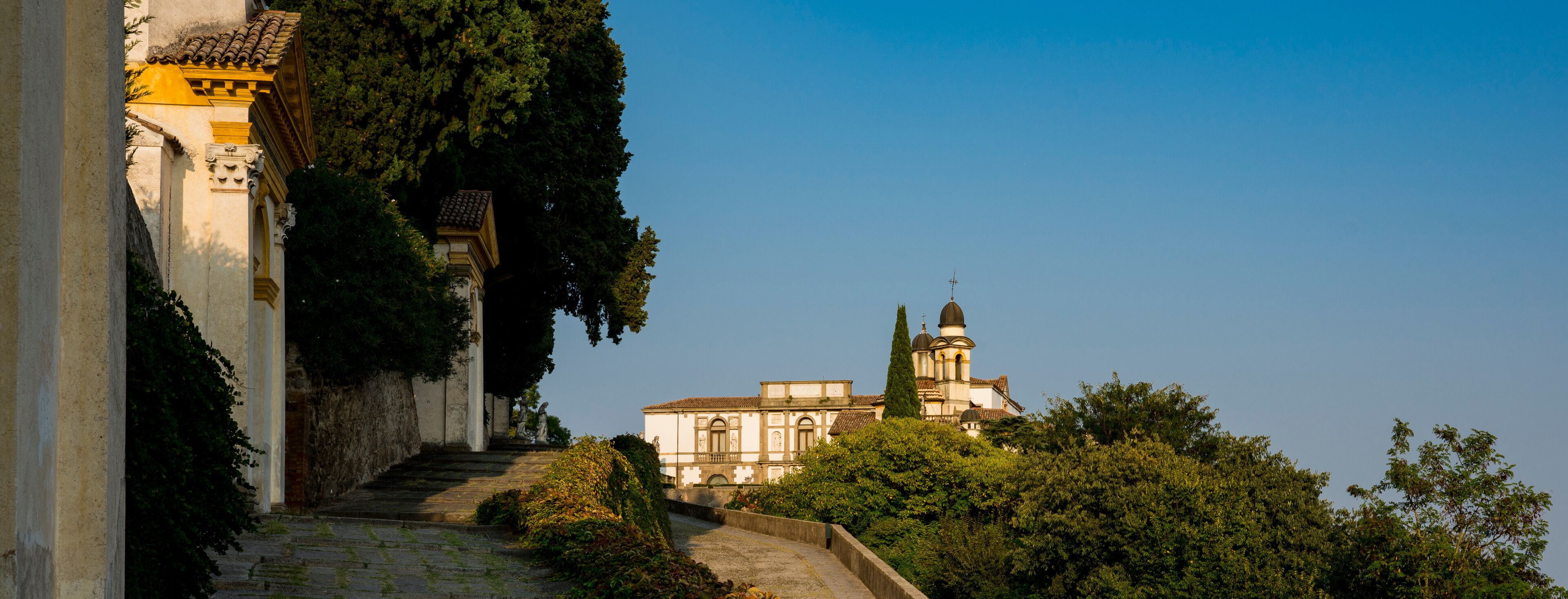 A stone staircase leading up to a building with a dome and bell tower, surrounded by lush greenery.