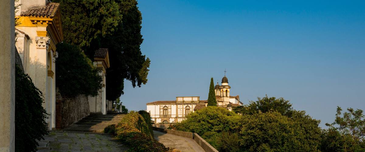 A stone staircase leading up to a building with a dome and bell tower, surrounded by lush greenery.