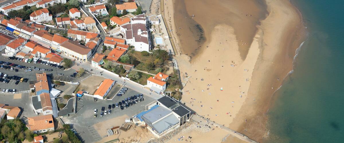 An aerial view of a coastal town with a beach, houses, and a pier.