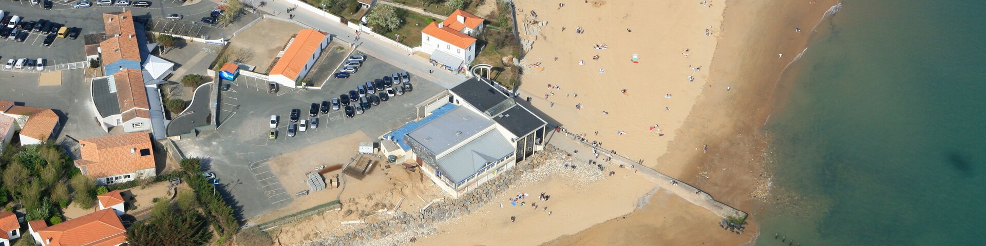 An aerial view of a coastal town with a beach, houses, and a pier.
