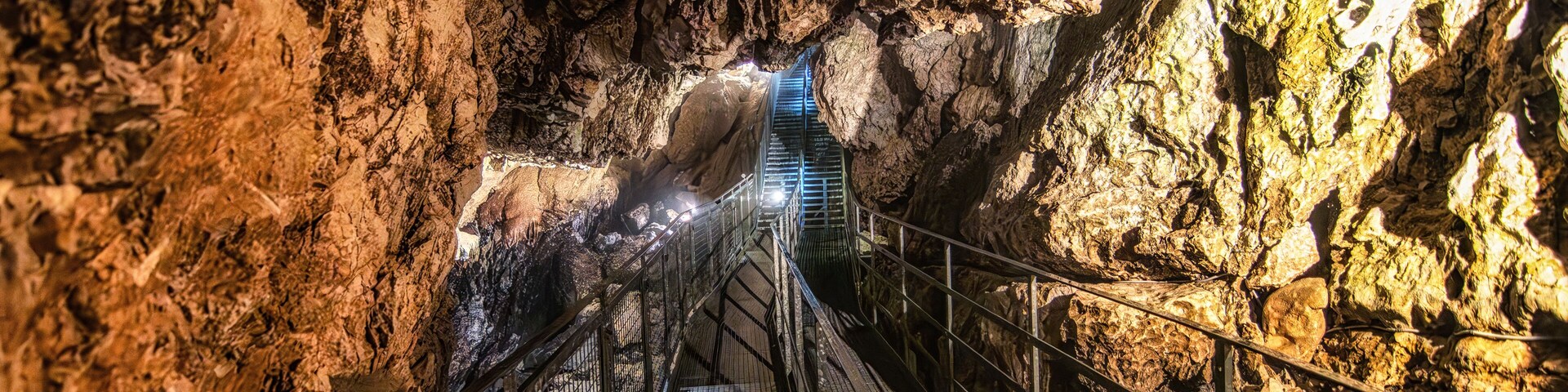 Una escalera de metal dentro de una cueva rocosa, con barandilla de metal.