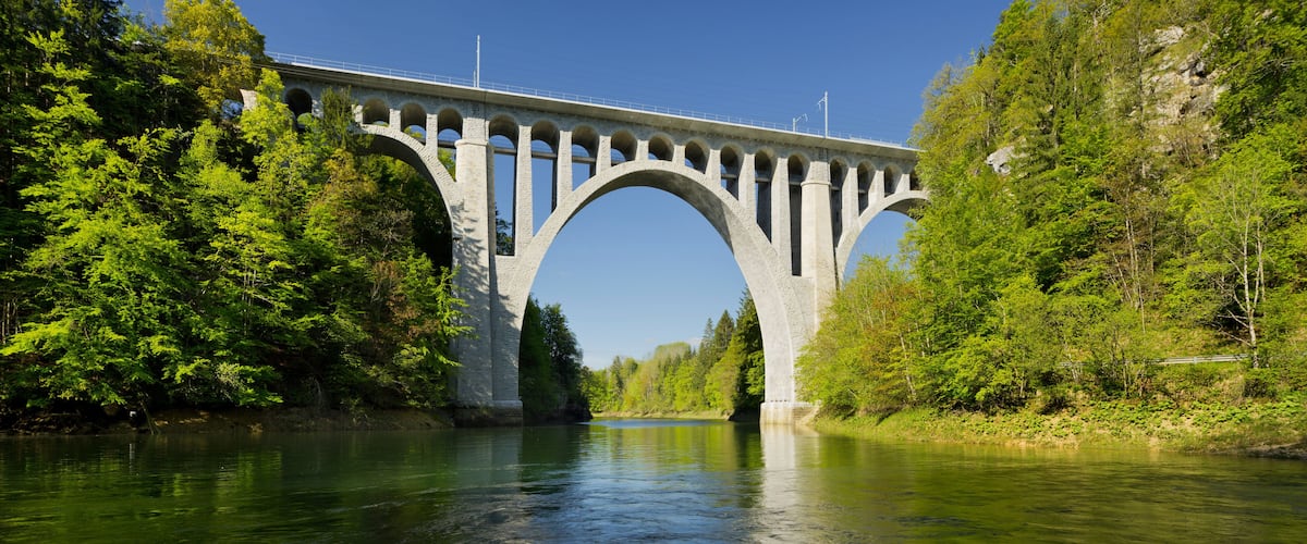 A stone bridge spanning a river, surrounded by dense green forest.