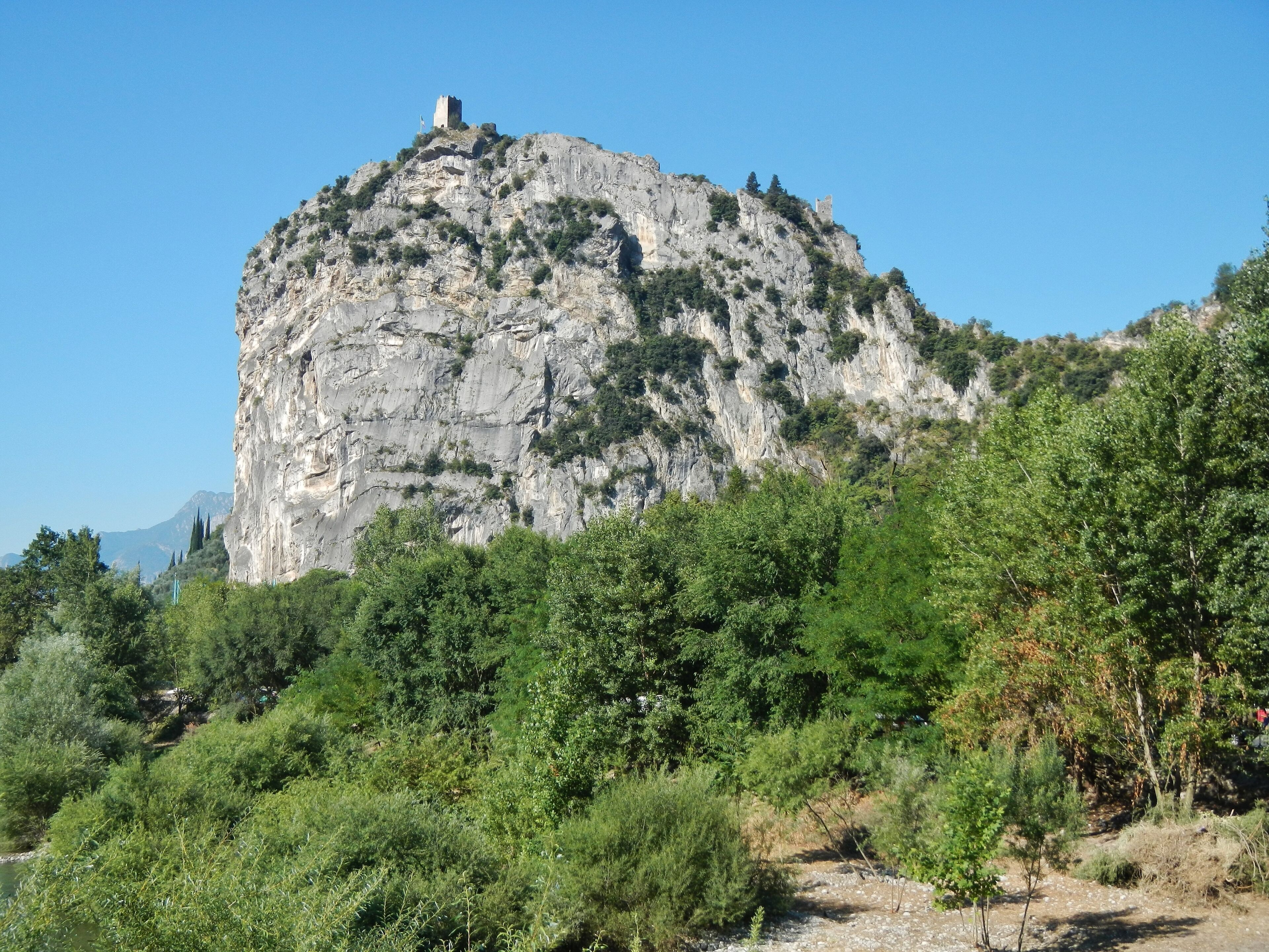 A rocky mountain with a castle on top, surrounded by dense green trees.