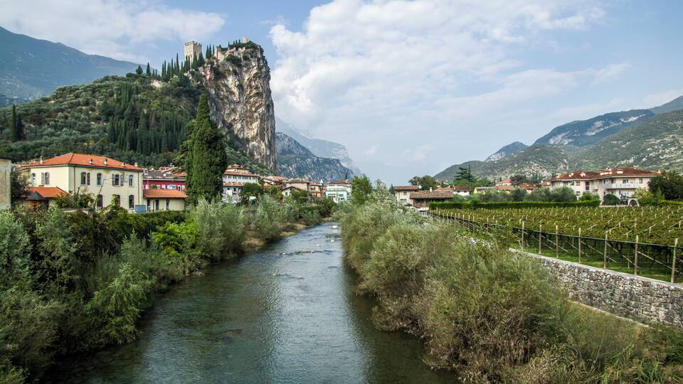 A river flowing through a town with buildings and a castle on a hill.