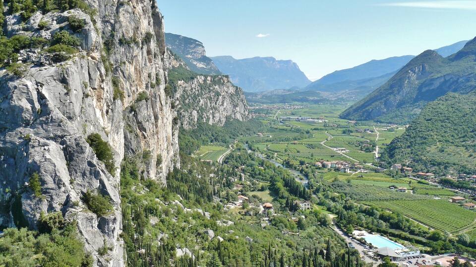 A mountainous landscape with a prominent rocky cliff, a river, and a valley with fields and buildings.