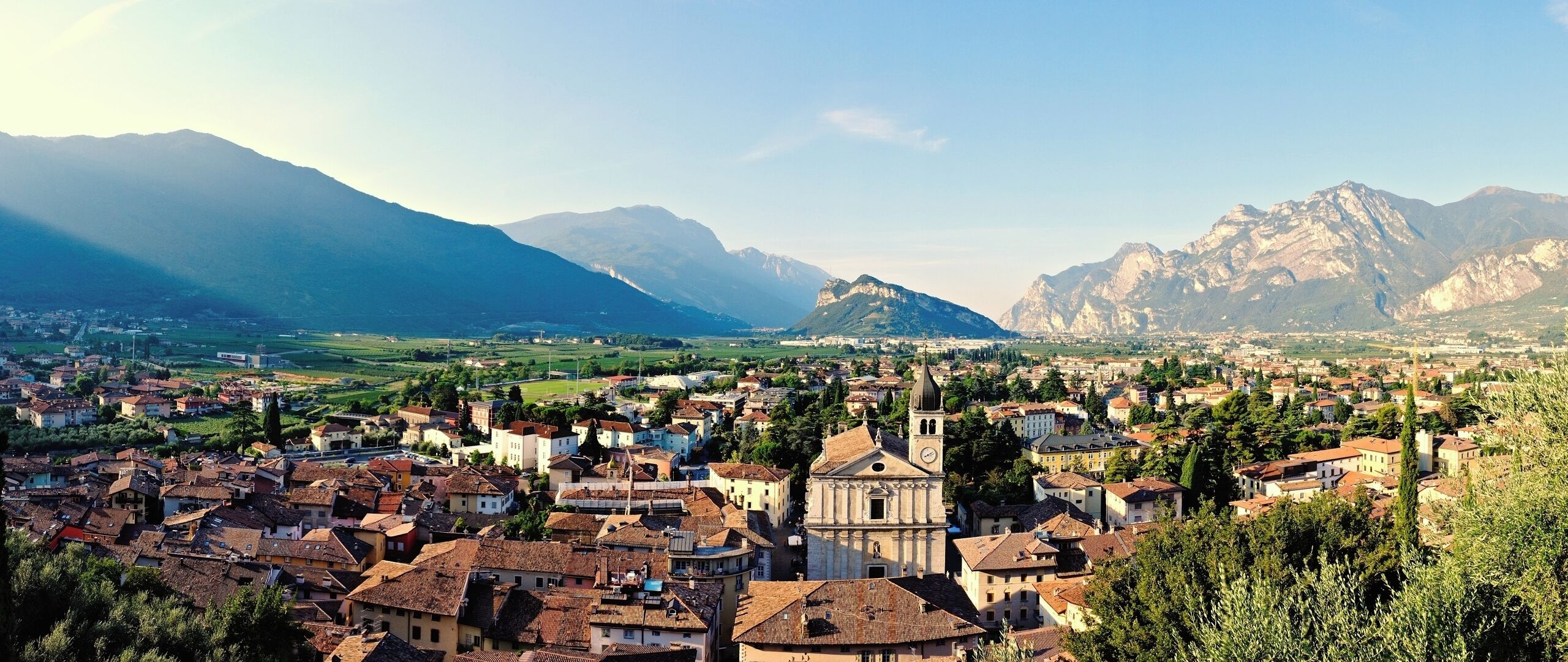 A town with a prominent church, surrounded by mountains and greenery.