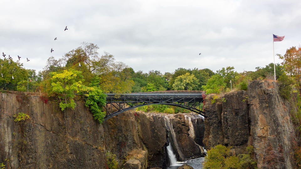 A bridge over a waterfall with a river below, surrounded by trees and cliffs.