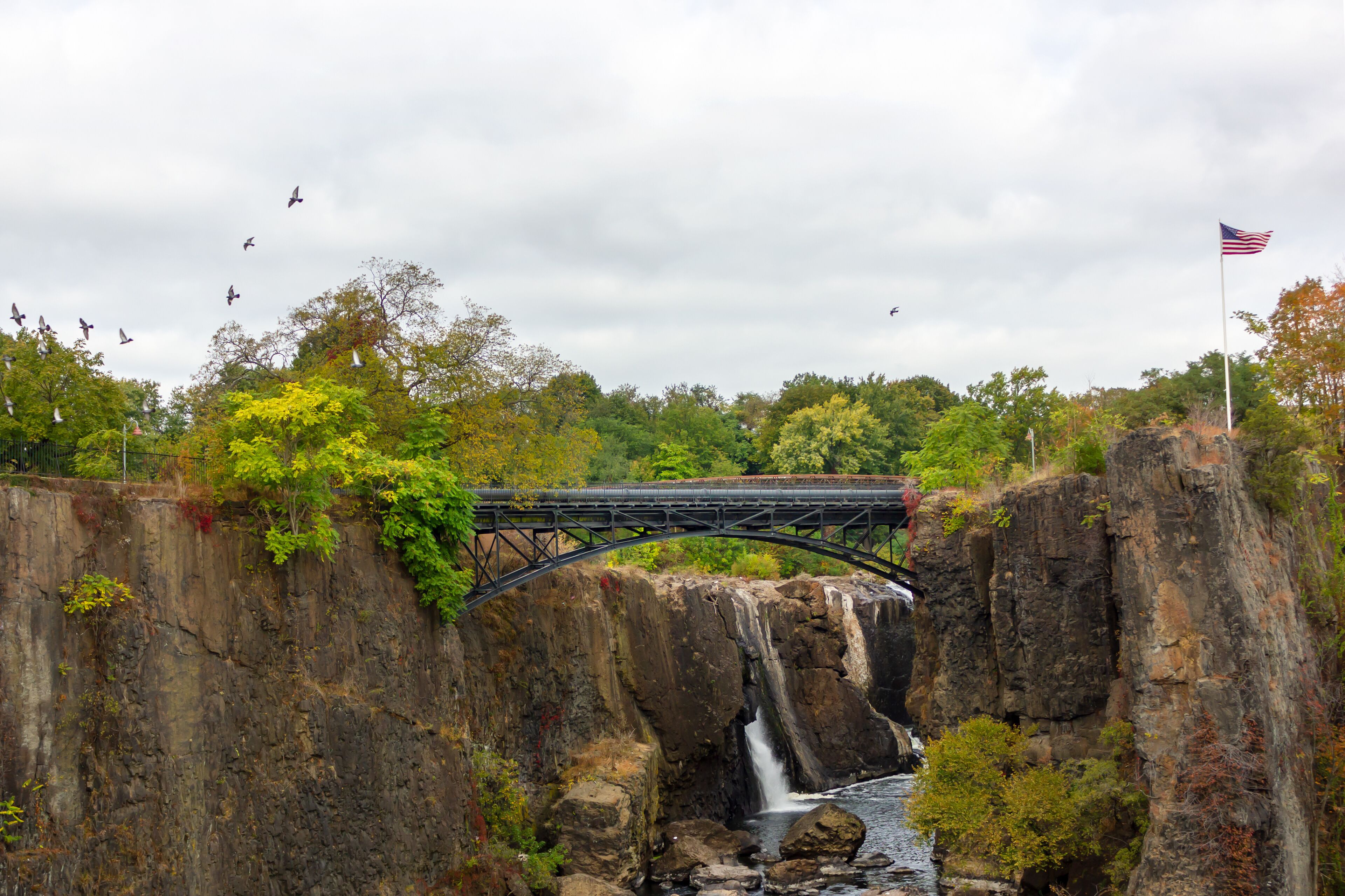 A bridge over a waterfall with a river below, surrounded by trees and cliffs.