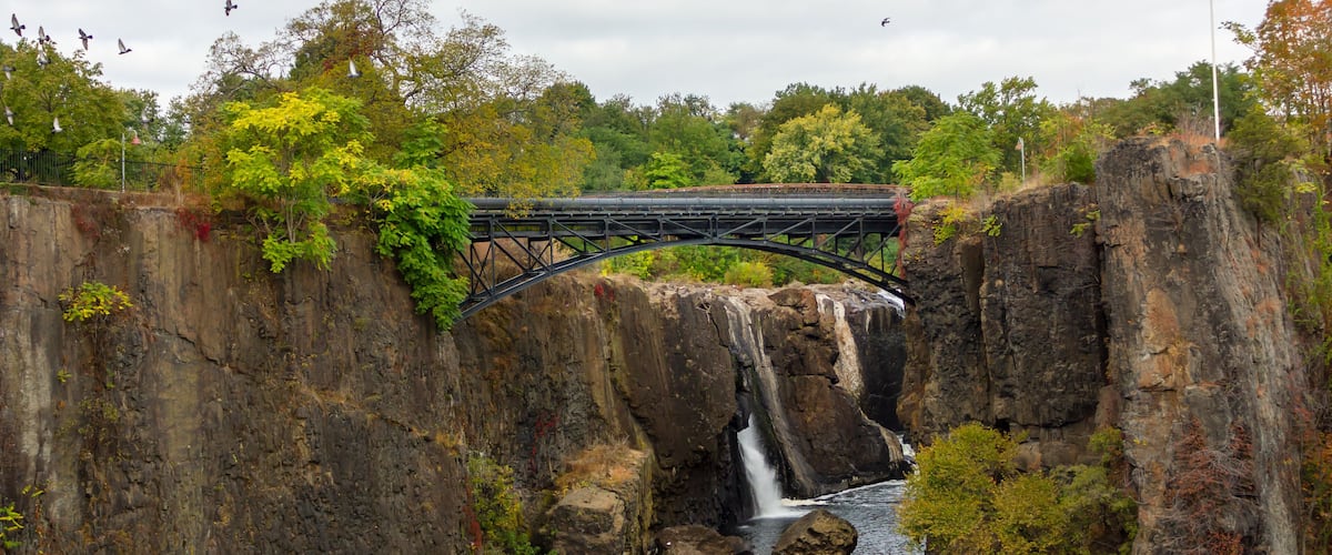 A bridge over a waterfall with a river below, surrounded by trees and cliffs.