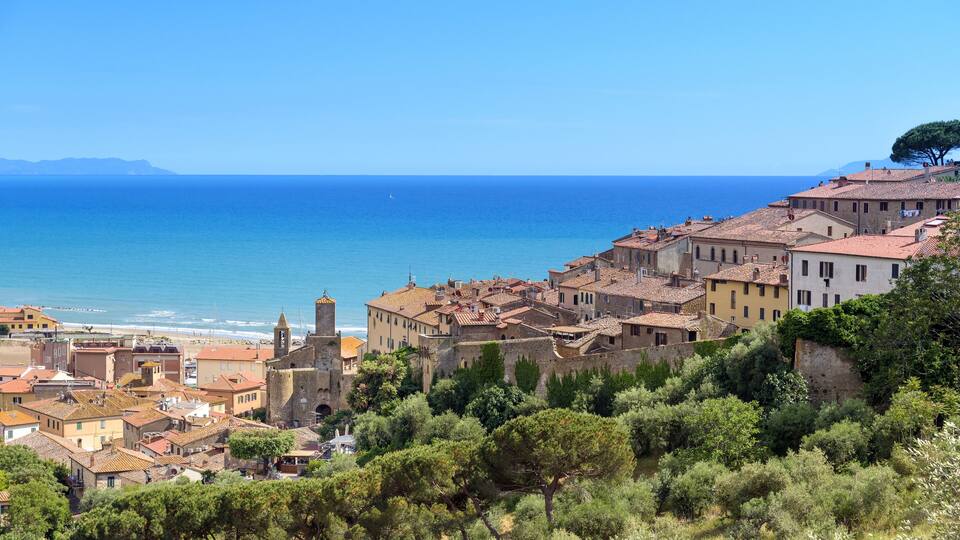 A coastal town with historic buildings, a clear blue sea, and lush greenery.