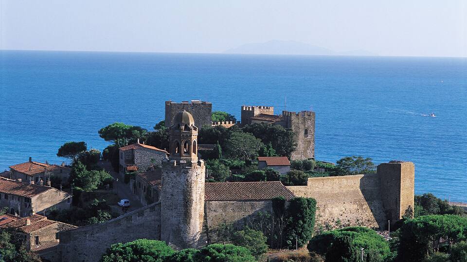 A coastal town with historic stone buildings and a prominent tower overlooking the sea.