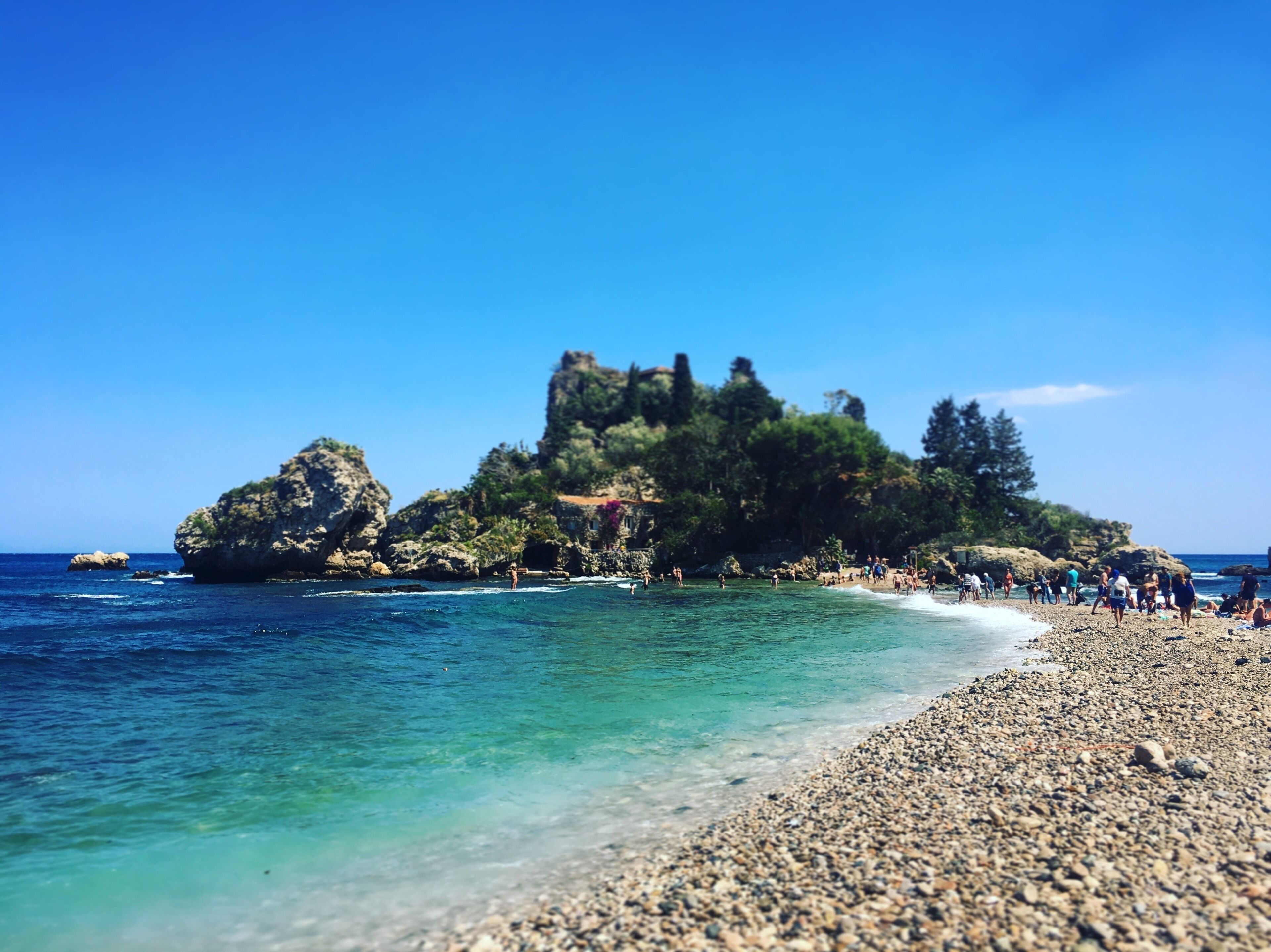 Uma ilha rochosa com águas turquesa cristalinas e uma praia de pedrinhas.