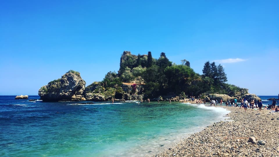 A rocky island with clear turquoise waters and a pebbly beach.