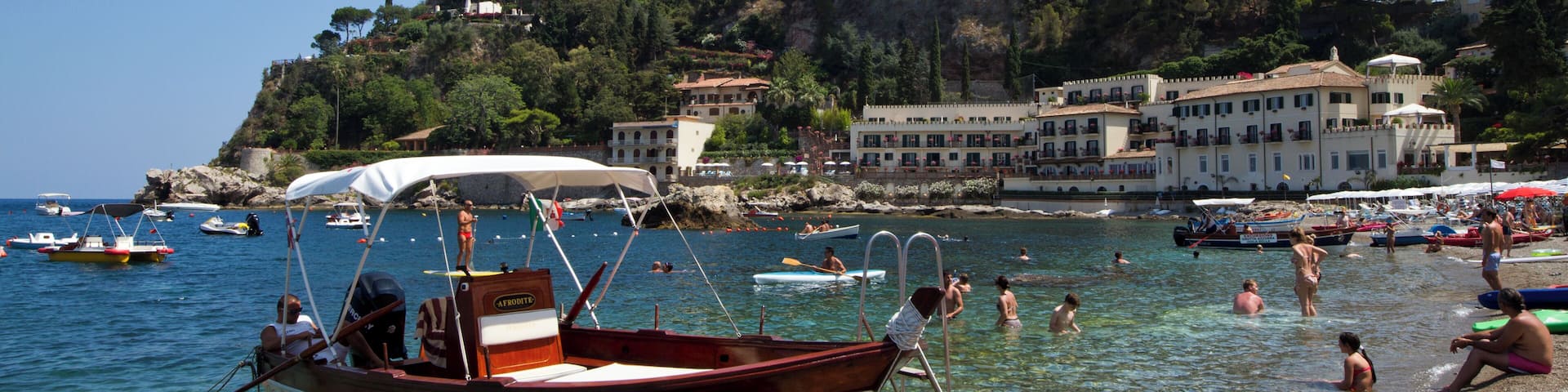 A coastal town with clear waters, boats, and people enjoying the beach.