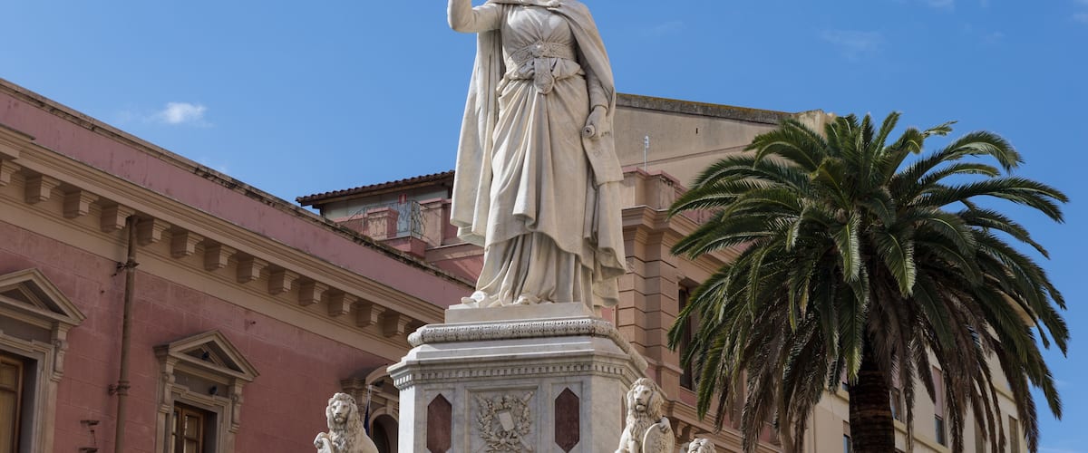 A statue of a woman with a raised hand, a palm tree, and a building with arched windows.