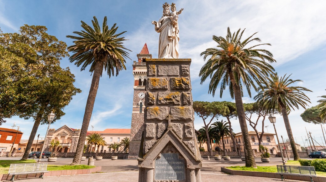 A monument with a statue, palm trees, and a building with a clock tower in the background.