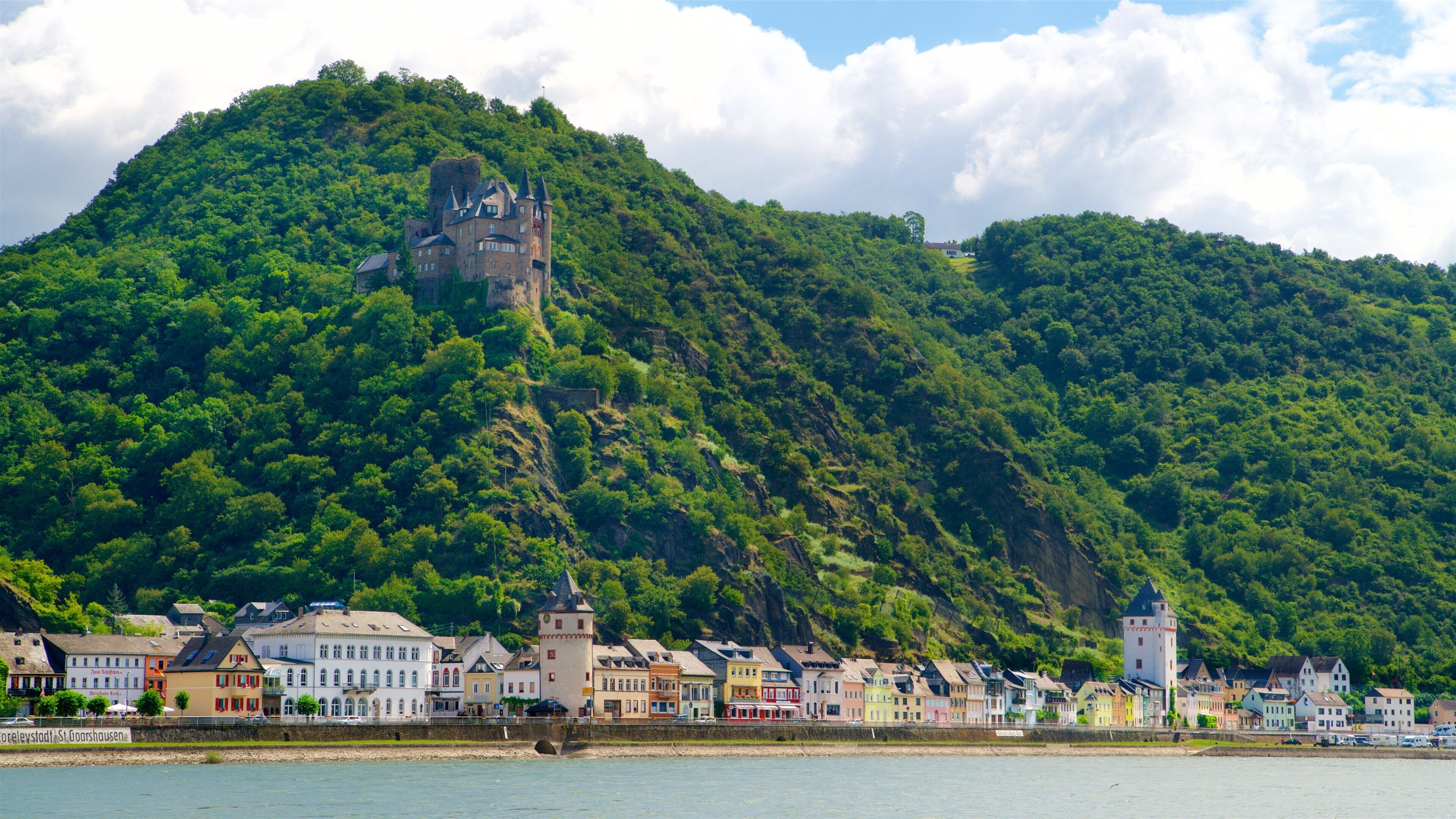 A castle on a hill, a river, and colorful buildings along the riverbank.