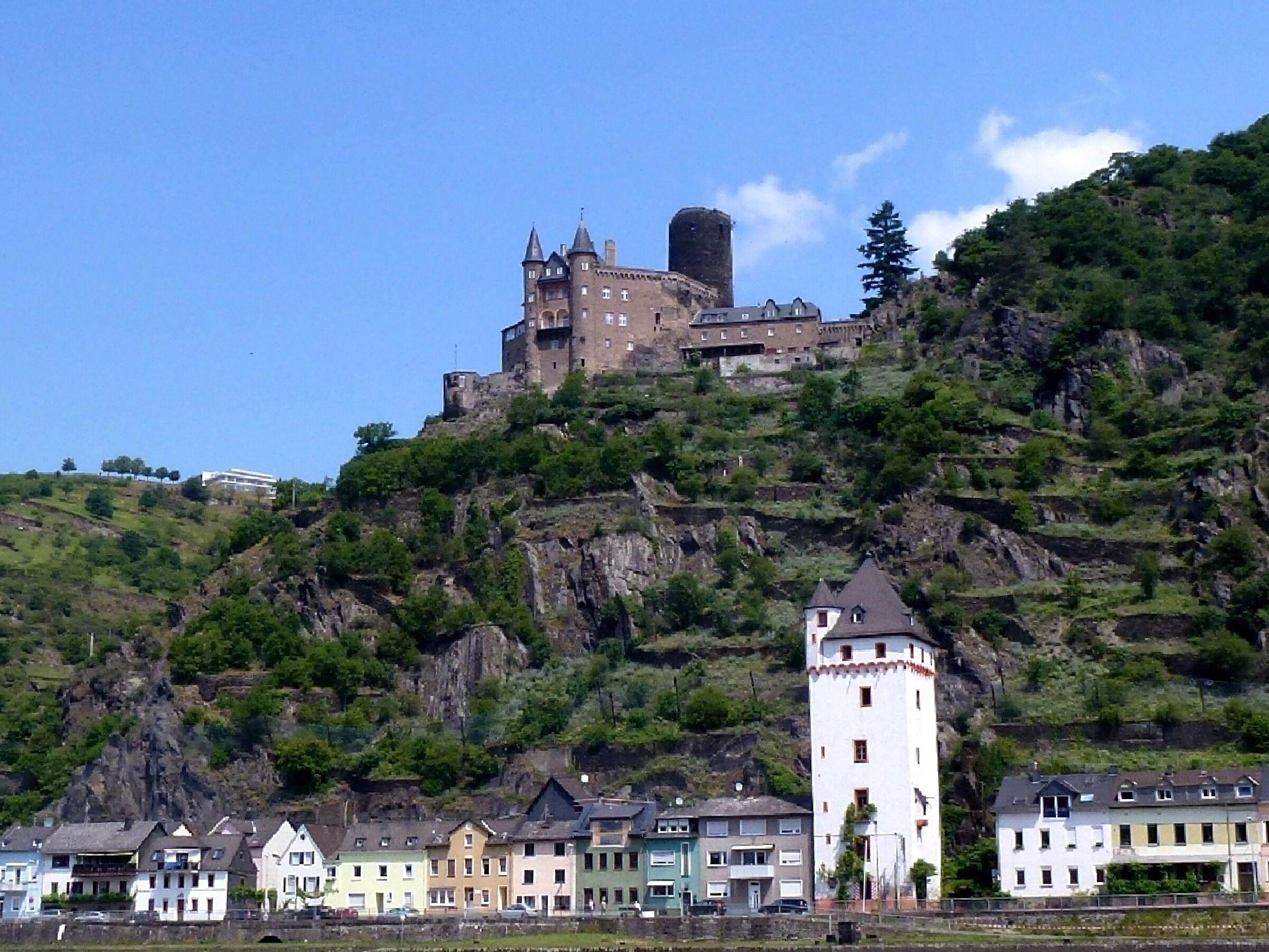 A castle on a hill with a tower, surrounded by colorful houses.
