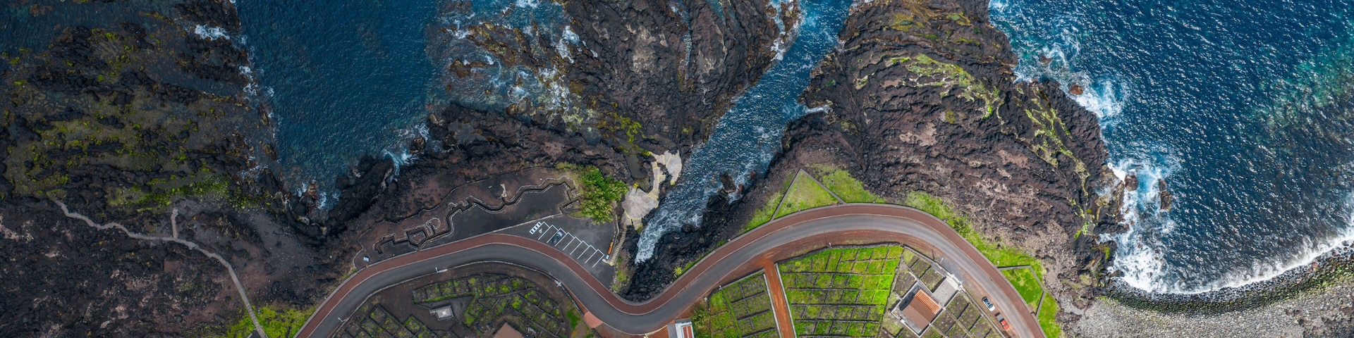 An aerial view of a coastal area with rocky cliffs, a winding road, and green fields.