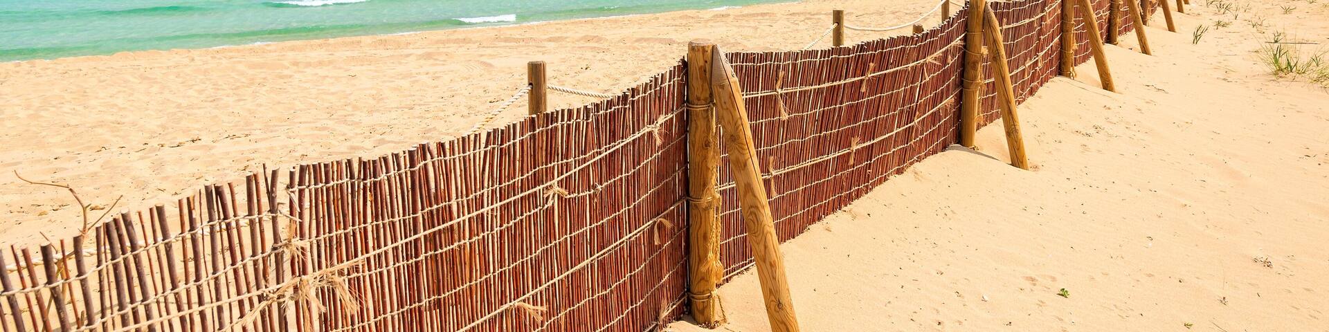 A beach with a bamboo fence, clear turquoise water, and a clear sky.