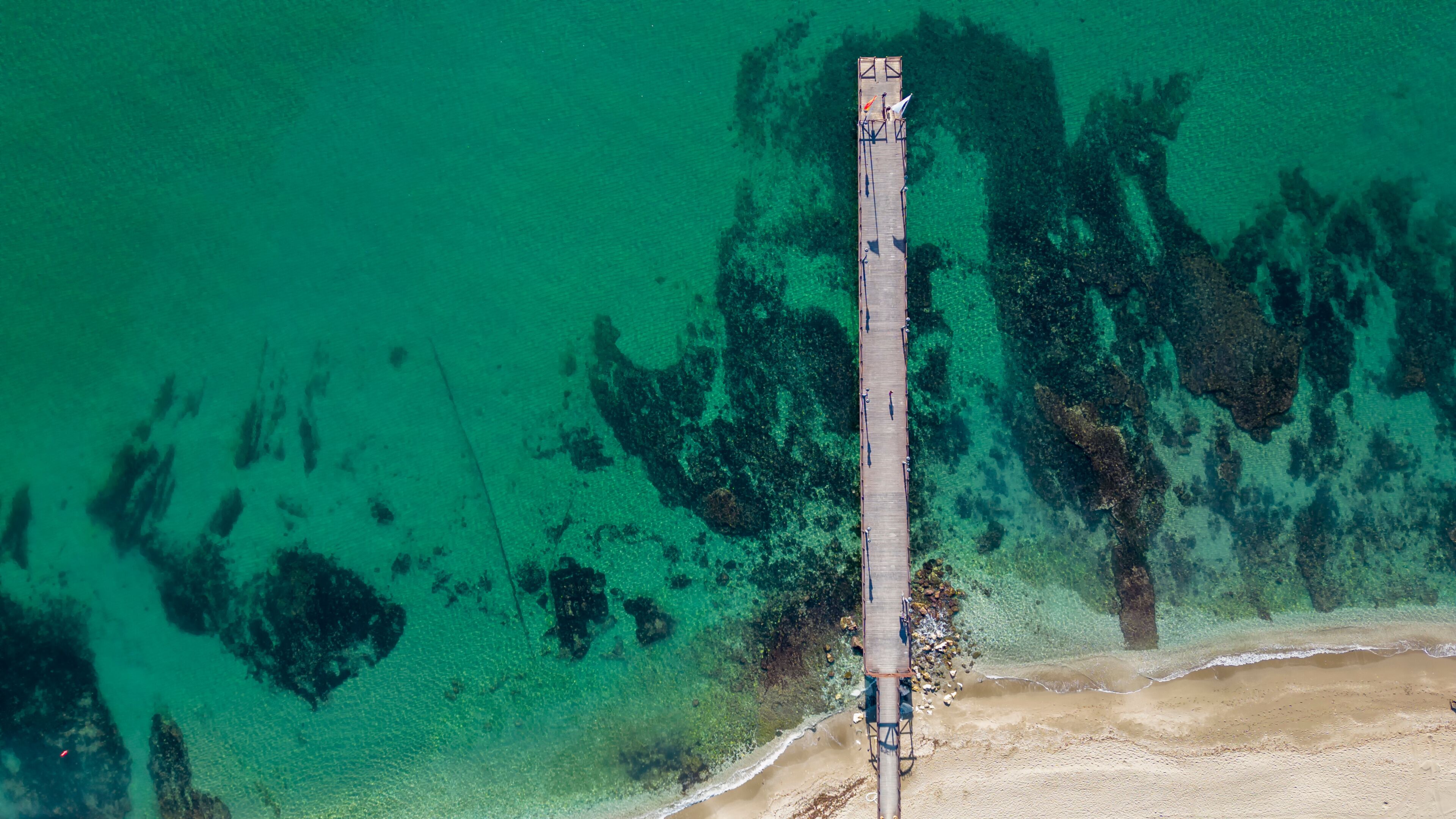 An aerial view of a pier extending into turquoise waters with clear visibility of underwater rock formations.