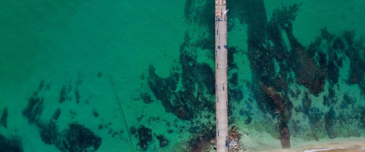 An aerial view of a pier extending into turquoise waters with clear visibility of underwater rock formations.