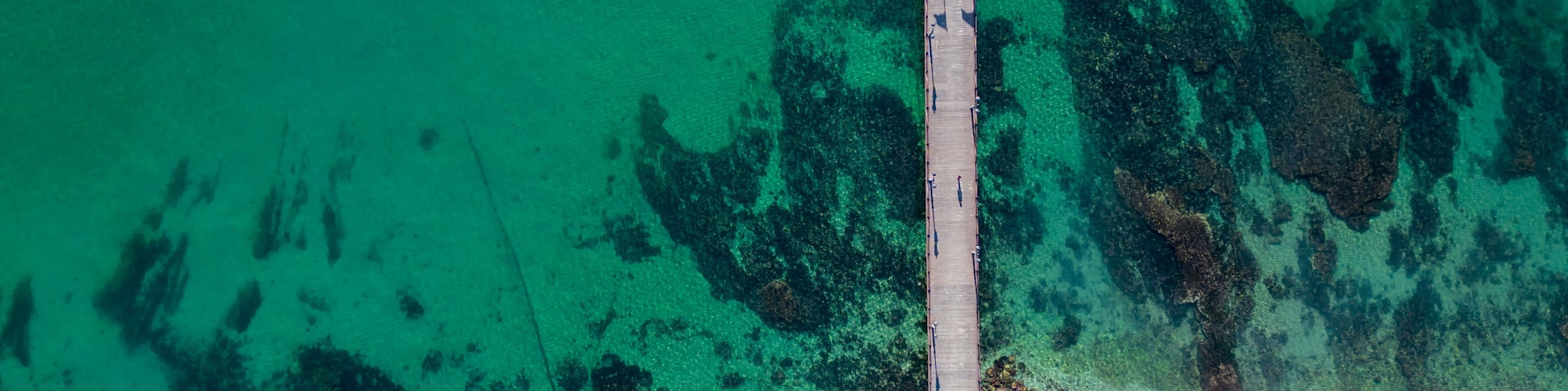 An aerial view of a pier extending into turquoise waters with clear visibility of underwater rock formations.