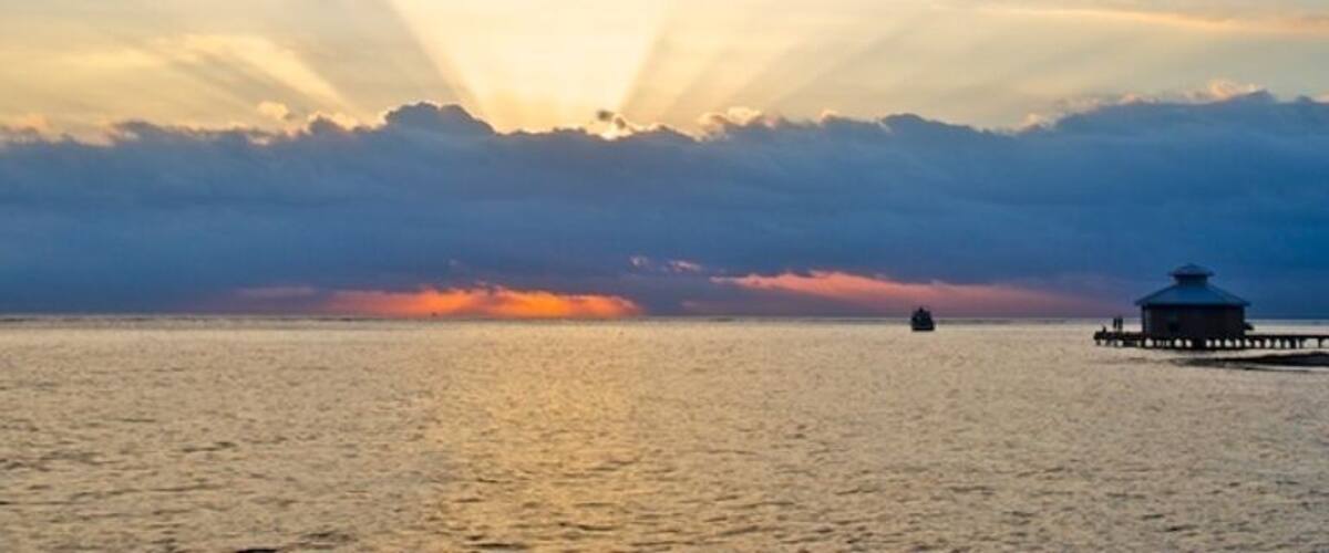 A sunset over a calm sea with a pier and a boat.