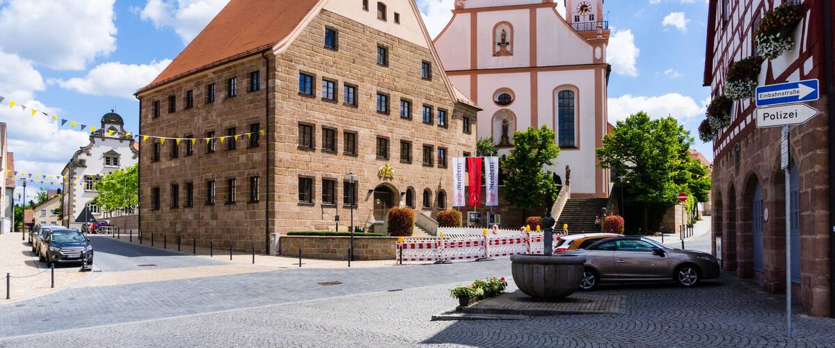 A historic town square with a church, a large stone building, and a car parked on the cobblestone street.